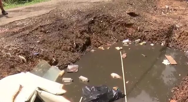 Vecindario de Alabama bajo riesgo sanitario por gran bache Gran bache profundo en un callejón urbano pavimentado con acumulación de escombros y daños en la acera.