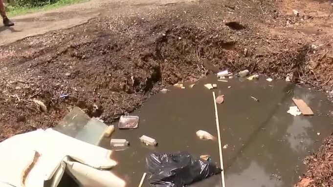Vecindario de Alabama bajo riesgo sanitario por gran bache Gran bache profundo en un callejón urbano pavimentado con acumulación de escombros y daños en la acera.