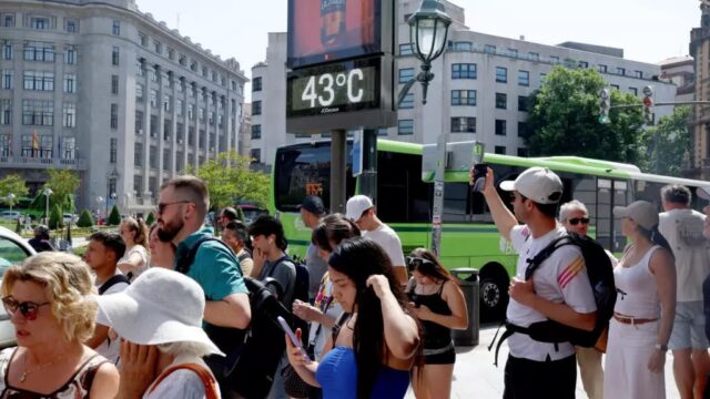 Termómetro urbano digital marcando temperaturas extremas bajo el sol en una plaza pública europea durante una ola de calor.