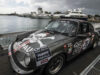 Rallye de la Cerámica se suspende tras trágico accidente Un coche clásico Porsche de rally gris con el logo de St. Pauli estacionado en un muelle náutico junto a yates.
