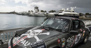Rallye de la Cerámica se suspende tras trágico accidente Un coche clásico Porsche de rally gris con el logo de St. Pauli estacionado en un muelle náutico junto a yates.