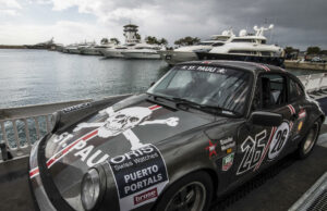 Rallye de la Cerámica se suspende tras trágico accidente Un coche clásico Porsche de rally gris con el logo de St. Pauli estacionado en un muelle náutico junto a yates.