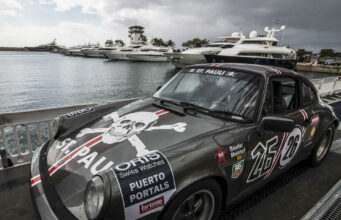 Rallye de la Cerámica se suspende tras trágico accidente Un coche clásico Porsche de rally gris con el logo de St. Pauli estacionado en un muelle náutico junto a yates.