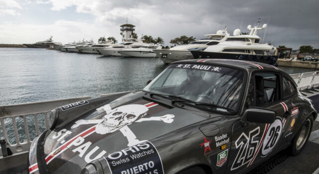 Rallye de la Cerámica se suspende tras trágico accidente Un coche clásico Porsche de rally gris con el logo de St. Pauli estacionado en un muelle náutico junto a yates.