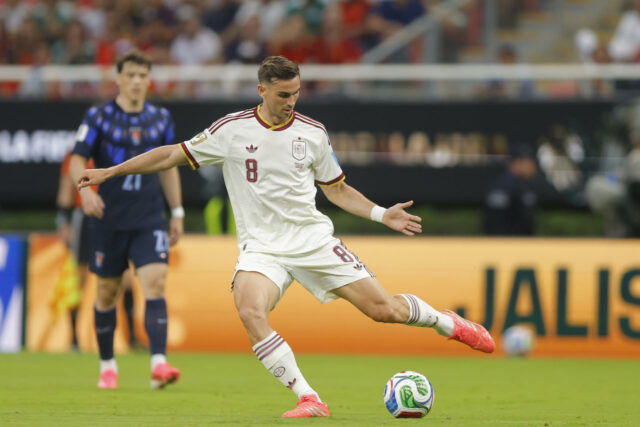 Álex Baena con el uniforme blanco de la selección española patea el balón durante el partido frente a Uruguay.