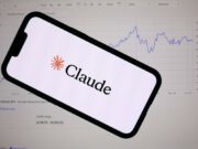 Anthropic lanza Claude Fable 5 con defensas de ciberseguridad Teléfono inteligente mostrando el logotipo de Anthropic Claude frente a una pantalla con gráficos financieros de bolsa.
