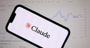 Anthropic lanza Claude Fable 5 con defensas de ciberseguridad Teléfono inteligente mostrando el logotipo de Anthropic Claude frente a una pantalla con gráficos financieros de bolsa.