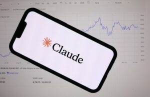 Anthropic lanza Claude Fable 5 con defensas de ciberseguridad Teléfono inteligente mostrando el logotipo de Anthropic Claude frente a una pantalla con gráficos financieros de bolsa.