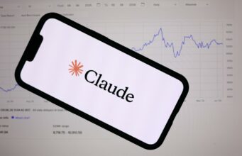 Anthropic lanza Claude Fable 5 con defensas de ciberseguridad Teléfono inteligente mostrando el logotipo de Anthropic Claude frente a una pantalla con gráficos financieros de bolsa.