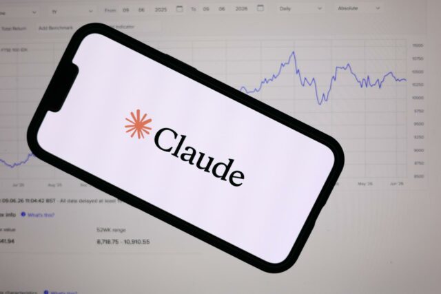 Teléfono inteligente mostrando el logotipo de Anthropic Claude frente a una pantalla con gráficos financieros de bolsa.