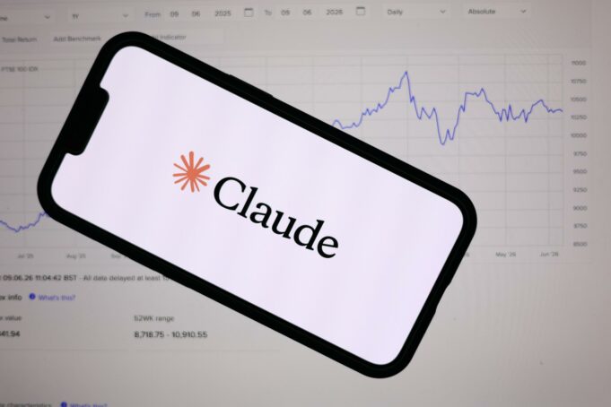 Anthropic lanza Claude Fable 5 con defensas de ciberseguridad Teléfono inteligente mostrando el logotipo de Anthropic Claude frente a una pantalla con gráficos financieros de bolsa.