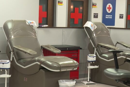 Donación de sangre en Alabama bajo alerta por escasez Sillones vacíos de color gris en una sala de donación de la Cruz Roja Americana con logotipos de cruces rojas al fondo.