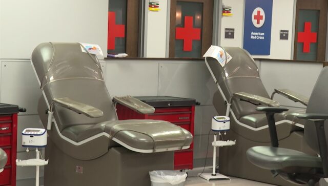 Sillones vacíos de color gris en una sala de donación de la Cruz Roja Americana con logotipos de cruces rojas al fondo.