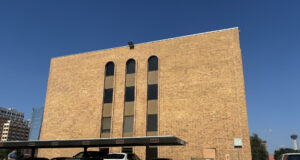 Cortes de inmigración aplican polémicas audiencias masivas Edificio de ladrillo marrón de la corte de inmigración en San Antonio con estacionamiento frontal de automóviles.