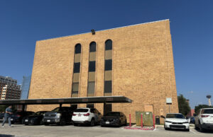 Cortes de inmigración aplican polémicas audiencias masivas Edificio de ladrillo marrón de la corte de inmigración en San Antonio con estacionamiento frontal de automóviles.