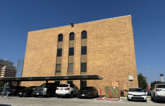 Cortes de inmigración aplican polémicas audiencias masivas Edificio de ladrillo marrón de la corte de inmigración en San Antonio con estacionamiento frontal de automóviles.