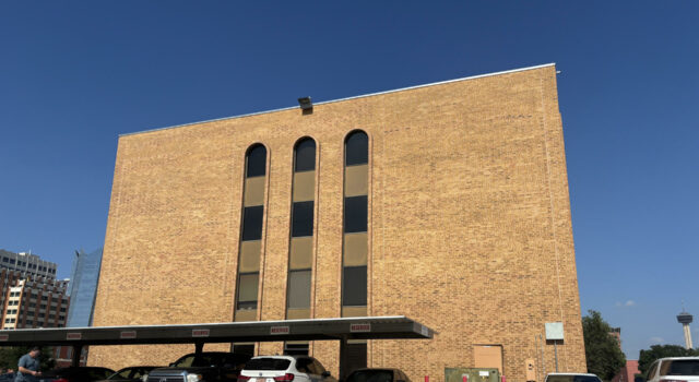 Cortes de inmigración aplican polémicas audiencias masivas Edificio de ladrillo marrón de la corte de inmigración en San Antonio con estacionamiento frontal de automóviles.