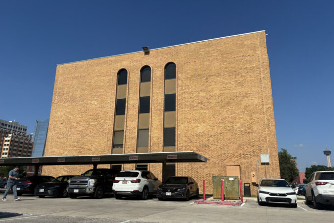 Cortes de inmigración aplican polémicas audiencias masivas Edificio de ladrillo marrón de la corte de inmigración en San Antonio con estacionamiento frontal de automóviles.