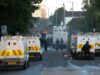 Disturbios en Belfast: Choques por el ataque de un refugiado Furgones blindados de la policía de Irlanda del Norte bloqueando una calle con humo y fuego de fondo durante los disturbios en Belfast.