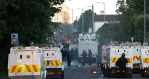 Disturbios en Belfast: Choques por el ataque de un refugiado Furgones blindados de la policía de Irlanda del Norte bloqueando una calle con humo y fuego de fondo durante los disturbios en Belfast.