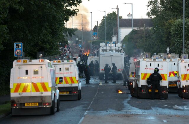 Segunda noche de disturbios en Belfast tras apuñalamiento de un hombre por un sudanés Furgones blindados de la policía de Irlanda del Norte bloqueando una calle con humo y fuego de fondo durante los disturbios en Belfast.