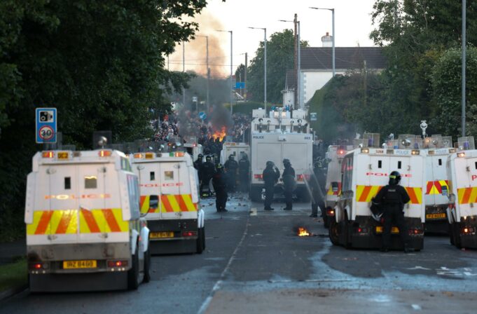 Disturbios en Belfast: Choques por el ataque de un refugiado Furgones blindados de la policía de Irlanda del Norte bloqueando una calle con humo y fuego de fondo durante los disturbios en Belfast.