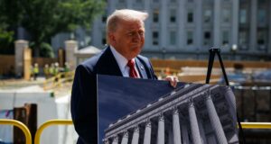 Donald Trump respalda a Abelardo de la Espriella en Colombia Donald Trump sonríe sosteniendo una fotografía de un edificio con columnas clásicas durante un evento de prensa exterior.