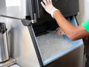 Inspección de alimentos en Birmingham provoca cierres temporales Un empleado con guantes de protección extrae hielo con una pala desde una máquina expendedora de acero inoxidable.