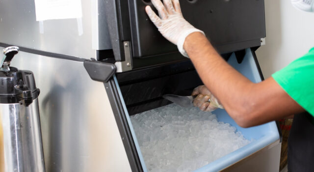 Inspección de alimentos en Birmingham provoca cierres temporales Un empleado con guantes de protección extrae hielo con una pala desde una máquina expendedora de acero inoxidable.
