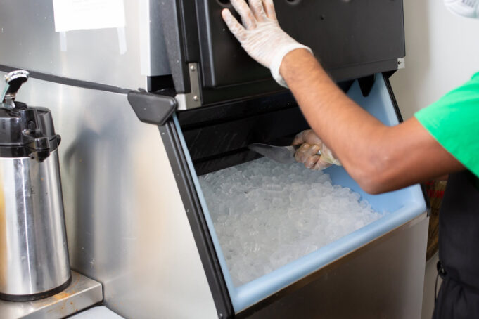 Inspección de alimentos en Birmingham provoca cierres temporales Un empleado con guantes de protección extrae hielo con una pala desde una máquina expendedora de acero inoxidable.