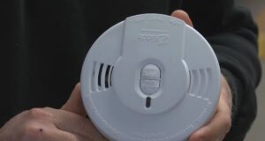 Detectores de humo gratis en Moody: cómo solicitarlos Manos de un bombero sosteniendo un detector de humo circular blanco de la marca Kidde para instalación gratuita en Moody.