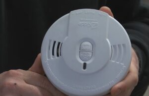 Detectores de humo gratis en Moody: cómo solicitarlos Manos de un bombero sosteniendo un detector de humo circular blanco de la marca Kidde para instalación gratuita en Moody.