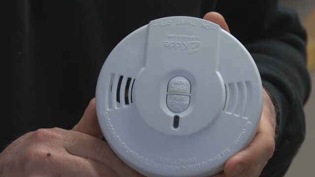 Manos de un bombero sosteniendo un detector de humo circular blanco de la marca Kidde para instalación gratuita en Moody.
