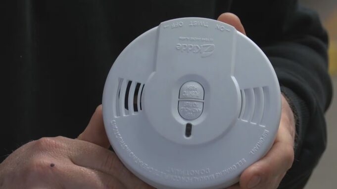 Detectores de humo gratis en Moody: cómo solicitarlos Manos de un bombero sosteniendo un detector de humo circular blanco de la marca Kidde para instalación gratuita en Moody.