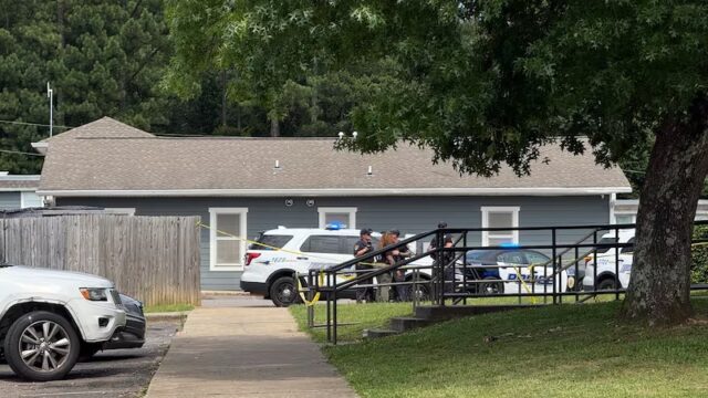Patrullas policiales y cinta de seguridad amarilla frente a una vivienda gris durante investigación en Birmingham.