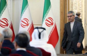 Acuerdo con EE.UU.: Irán frena la expectativa de Donald Trump Funcionario iraní camina en una sala de reuniones con banderas oficiales de Irán al fondo.