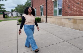 Maestra de DLI regresa a Escuelas de Birmingham Maestra de DLI Reiniela Ortiz camina frente al edificio de ladrillo rojo de una escuela en Alabama.