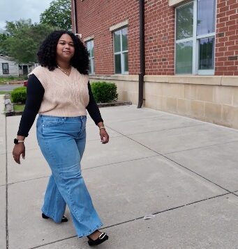 Maestra de DLI regresa a Escuelas de Birmingham Maestra de DLI Reiniela Ortiz camina frente al edificio de ladrillo rojo de una escuela en Alabama.