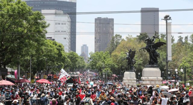 Maestros en México inician huelga y cercan el Zócalo Multitud de maestros en México marchando por una avenida con banderas en protesta contra el gobierno.