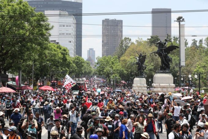 Maestros en México inician huelga y cercan el Zócalo Multitud de maestros en México marchando por una avenida con banderas en protesta contra el gobierno.