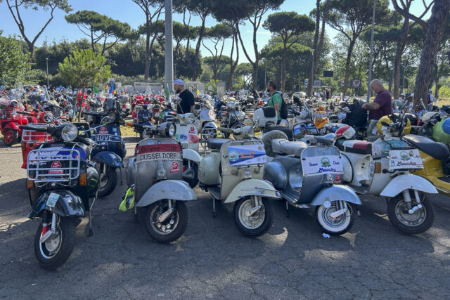 Gran concentración de motonetas Vespa de clubes internacionales estacionadas al aire libre durante el aniversario en Roma.