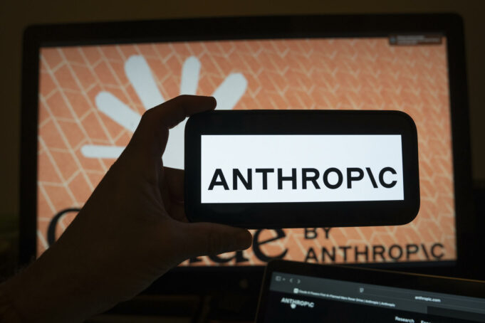 Modelos de IA en EE. UU. serán testados bajo nueva orden Mano sosteniendo un teléfono móvil con el logotipo de Anthropic frente a una pantalla de ordenador con la interfaz del software.