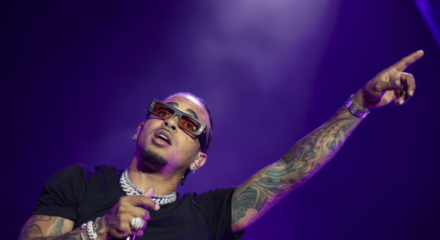 Gira de Ozuna 2026 arranca con espectacular concierto en Ibiza El cantante de reggaetón Ozuna cantando con micrófono y señalando hacia arriba con gafas de sol oscuras en concierto.