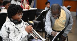 Programa de verano en Alabama impulsa arte y música Estudiante tocando la trompeta junto a un instructor de música que señala una partitura en el campamento June Tunes.