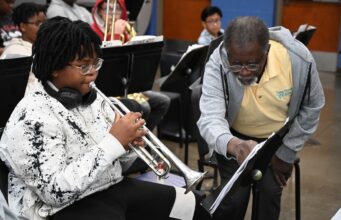 Programa de verano en Alabama impulsa arte y música Estudiante tocando la trompeta junto a un instructor de música que señala una partitura en el campamento June Tunes.
