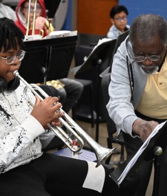 Programa de verano en Alabama impulsa arte y música Estudiante tocando la trompeta junto a un instructor de música que señala una partitura en el campamento June Tunes.
