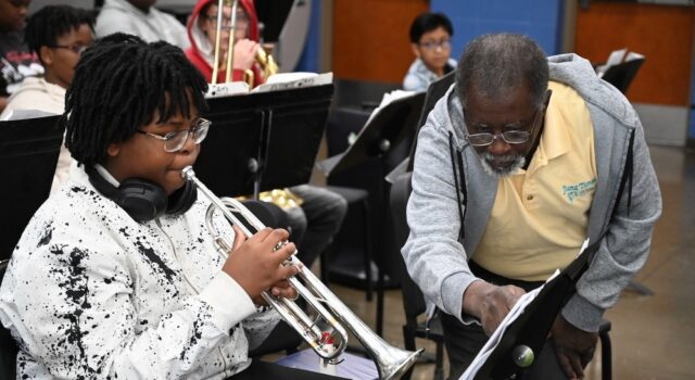 Programa de verano en Alabama impulsa arte y música Estudiante tocando la trompeta junto a un instructor de música que señala una partitura en el campamento June Tunes.