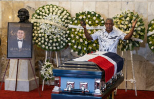 Muerte de Alex Bueno: El Teatro Nacional despide al cantante Capilla ardiente de Alex Bueno con su féretro cubierto por la bandera dominicana y arreglos florales en su honor.
