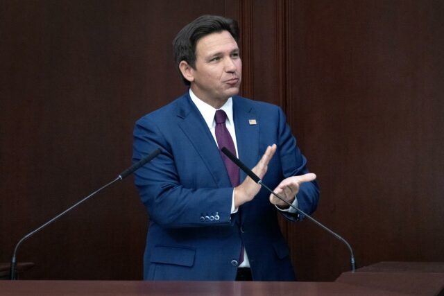 El gobernador de Florida Ron DeSantis con traje azul en un podio hablando sobre la reducción de impuestos inmobiliarios.