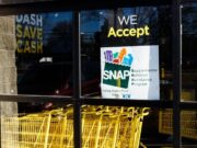 SNAP en Alabama sufrirá recortes por nueva ley federal Letrero oficial del programa SNAP en la ventana de un supermercado con carritos de compra amarillos en Alabama.